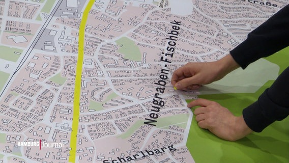Ein Mann setzt eine Markierung auf einen großen Stadtplan von Neugraben. © Screenshot 