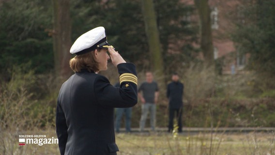 Eine Frau in der Uniform der Deutschen Marine von schräg hinten zu sehen, sie salutiert. © Screenshot 