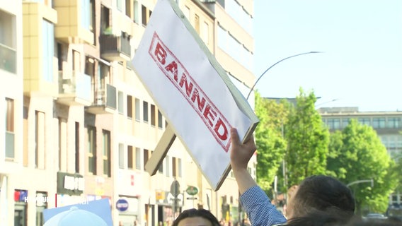 Schilder mit der Aufschrift "Banned" werden bei einer Versammlung von Islamisten in die Luft gehalten. © Screenshot 