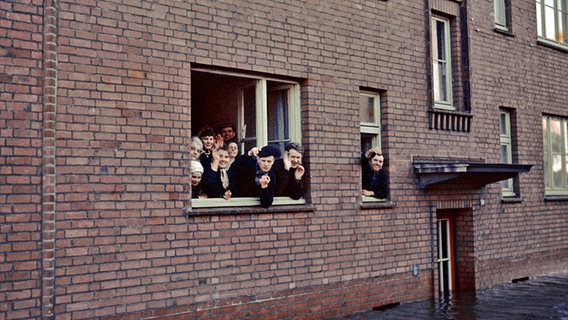 Menschen schauen aus einer Wohnung im überschwemmten Hamburg-Wilhelmsburg 1962. © NDR Foto: Hildegard Westphal