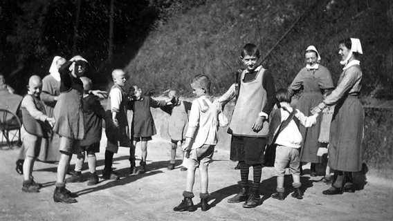 Geistig behinderte Kinder spielen mit zwei Diakonieschwestern um 1930 Ringelreihen. © dpa - Report 