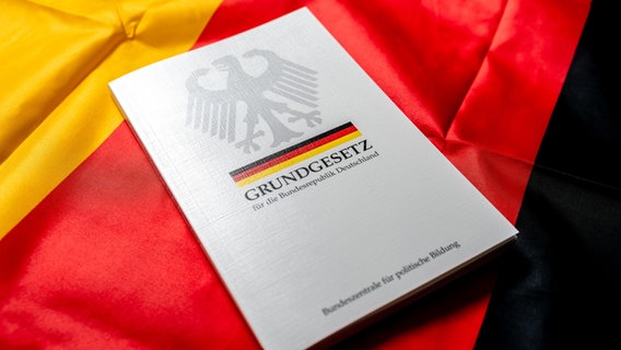 Ein Grundgesetz der Bundesrepublik Deutschland liegt auf einer deutschen Flagge. © picture alliance / CHROMORANGE | Michael Bihlmayer 