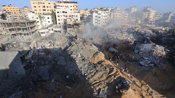 Menschen stehen in Gaza-Stadt nach israelischen Angriffen zwischen Trümmerhaufen. © dpa Foto: Saeed Jaras