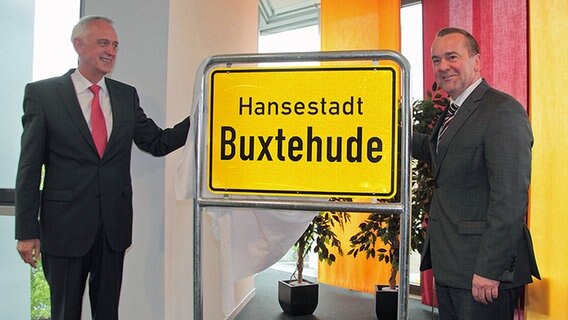 Jürgen Badur (parteilos), Bürgermeister von Buxtehude, und Boris Pistorius (SPD), niedersächsischer Innenminister, stehen neben einem Ortseingangsschild der Hansestadt Buxtehude. © Stadt Buxtehude 