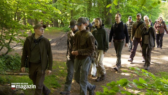 Mehrere Menschen in Jagdkleidung gehen durch einen Wald © NDR Foto: NDR Screenshot