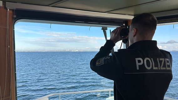 Ein Polizist blickt mit einem Fernglas aufs Meer. © NDR Foto: Hauke Bülow