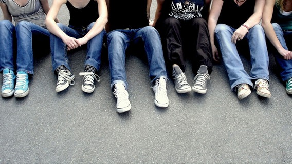 Jugendliche in Jeans und Turnschuhen sitzen nebeneinander © photocase 