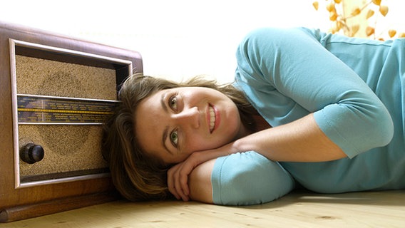 Junge Frau liegt auf dem Boden neben einem alten Radiogerät, hört zufrieden zu. © picture-alliance / KPA/Thomas Foto: KPA/Thomas