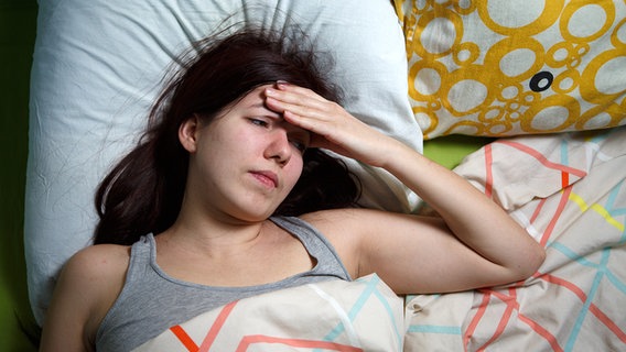 Junge Frau im Bett schaut verzweifelt und legt die Hand gegen die Stirn. © Fotolia.com Foto: Sergey