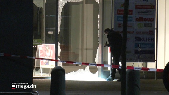 Ein Mann mit einer Taschenlampe steht vor einer zerstörten Glasscheibe. © Screenshot 