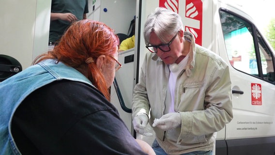 Ein Arzt hilft einer obdachlosen Frau vor dem Krankenmobil der Caritas © Screenshot 