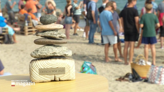 Ein Pokal aus Steinen mit der Aufschrift "Ditsch WM 2023" steht an einem Strand © Screenshot 