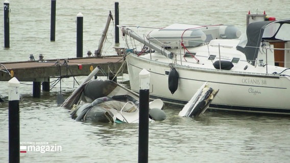 An einem Steg: Ein noch schwimmendes Segelboot, daneben schaut ein gesunkenes Boot kaum mehr aus dem Wasser. © Screenshot 