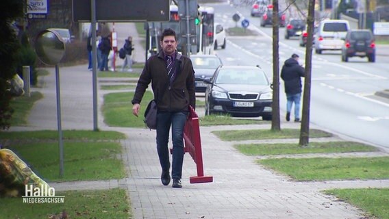 Melbeck's Bürgermeister Christoph Kleineberg trägt einen roten Gartenzaun zu einem offenen Bürgergespräch. © Screenshot 