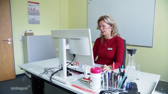 Eine Frau im roten Pullover sitzt am Schreibtisch und arbeitet am PC. © Screenshot 