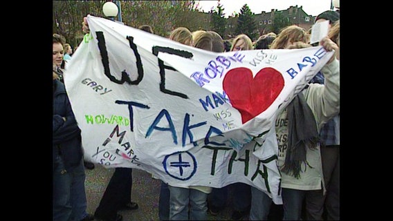 Jugendliche halten ein bunt bemaltes Banner mit der Aufschrift: "We love Take That". © Screenshot 