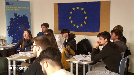 Jungendliche sitzen in einem Raum unter einer Europaflagge. © Screenshot 