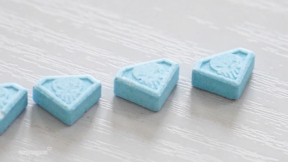 Blaue Ecstasy-Pillen mit Totenkopf-Prägung liegen nebeneinander auf einem Tisch. © Screenshot 