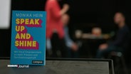 Ein Buch mit dem Titel "speak up and shine" steht auf einem Tisch. © Screenshot 