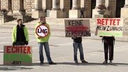 Vier Menschen haben Schilder in der Hand, die sich gegen die LNG-Pipeline richten. © Screenshot 