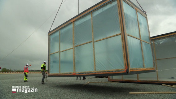 Arbeiter auf einer Baustelle dirigieren, wo ein Container abgesetzt werden soll. © Screenshot 