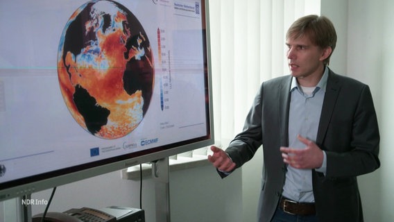 Axel Andersson vom Deutschen Wetterdienst neben einer Grafik, die auf einer Weltkugel die Temperaturen der Weltmeere zeigt. © Screenshot 