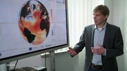 Axel Andersson vom Deutschen Wetterdienst neben einer Grafik, die auf einer Weltkugel die Temperaturen der Weltmeere zeigt. © Screenshot 