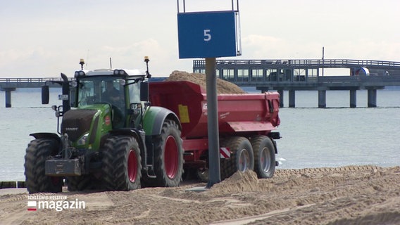 Ein Traktor fährt mit einer Ladung Sand am Strand entlang. © Screenshot 
