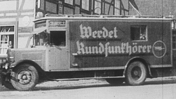 Histprisches Schwarz-Weiß-Bild: Ein Lkw mit der Aufschrift "Werdet Rundfunkhörer" fährt durch eine Straße © Screenshot 