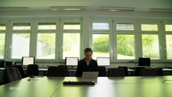 Ein Mann sitzt in einem großen Büro vor einem Laptop. © Screenshot 