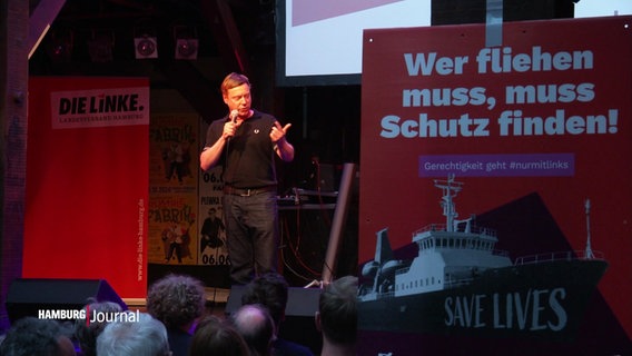 Der Linken-Politiker Martin Schirdewan spricht auf einer Bühne, hinter ihm Aufsteller mit Slogans seiner Partei. © Screenshot 