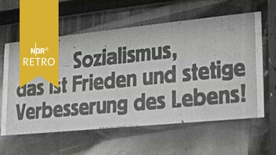 Schild in einem Schaufenster mit der Aufschrift "Sozialismus, das ist Frieden und stetige Verbesserung des Lebens!"  