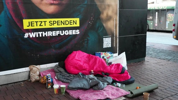 Ein Schlafsack liegt auf dem Boden vor einem Plakat, Symbolbild Obdachlosigkeit © Screenshot 