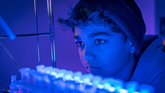Hakim ist in einem Labor mit blauem Licht. © NDR/ Letterbox Foto: Boris Laewen