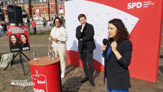 Europaabgeordnete Delara Burkhard spricht bei einer Wahlkampfveranstaltung am Kieler Hauptbahnhof neben Kevin Kühnert und Serpil Medyatli. © NDR 