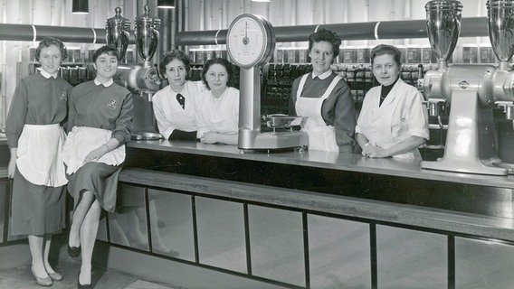 Filial-Mitarbeiterinnen von Tchibo in Kaiserslautern 1958 mit Mühlen und Waage. Im Hintergrund stapeln sich die 250g Päckchen Gold Mocca. © picture alliance/dpa/Tchibo 