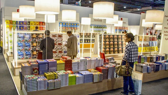 Eine Frau und zwei Männer betrachten die Bücherauswahl an Regalen voller Bücher und auf Stapeln - Bild auf der Buchmesse Frankfurt © imago/Rupert Oberhäuser Foto: Rupert Oberhäuser