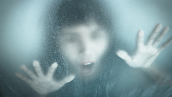 Eine panische Gestalt schaut durch eine Scheibe aus Riffelglas. © fotolia Foto: chainat