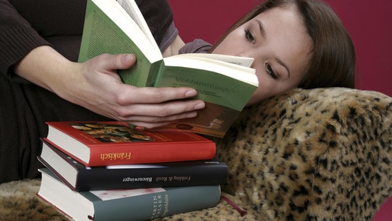 Eine Jugendliche liegt auf einer Couch und liest in einem Schulbuch. © picture alliance/imageBROKER Foto: Sonja Krebs