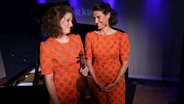 Zwei Frauen in orange stehen nebeneinander und lachen sich an. © Claudius Hinzmann / NDR Foto: Claudius Hinzmann / NDR