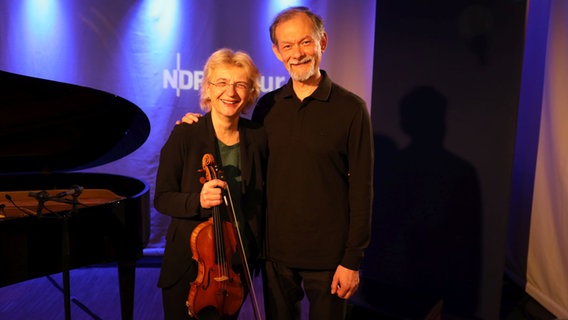 Eine Frau mit einer Geige in der Hand steht neben einem größeren Mann. © Ekaterina Shurygina / NDR Foto: Ekaterina Shurygina / NDR