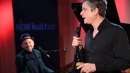 Ein Mann mit schwarzem Hemd singt und ein anderer sitzt links neben ihm am Flügel. © Claudius Hinzmann / NDR Foto: Claudius Hinzmann / NDR