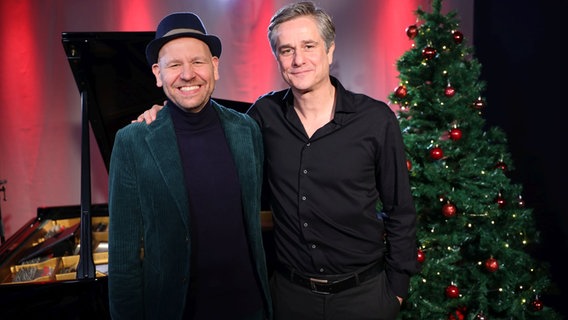 Zwei Männer stehen nebeneinander, rechts neben ihnen steht ein geschmückter Weihnachtsbaum. © Claudius Hinzmann / NDR Foto: Claudius Hinzmann / NDR