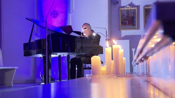 Ein Mann sitzt an einem Flügel, im Vordergrund stehen Kerzen © NDR 