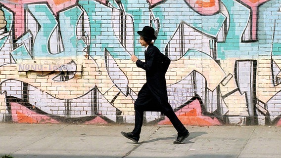 Ein junger orthodoxer Jude läuft an einer mit einem Grafitti bemalten Häuserwand in Williamsburg/ Brooklyn entlang. © imago/ Lem 