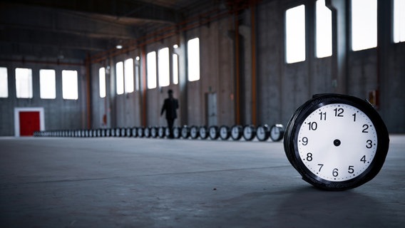 Eine Reihe von Uhren steht in einem leeren Fabrikgebäude. Eine zeigerlose Uhr ist frontal zu sehen. © Roberto Agagliate / photocase.de Foto: Roberto Agagliate