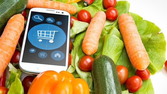 Ein Smartphone mit Einkaufswagensymbol zwischen Lebensmitteln. © fotolia.com Foto: Spectral-Design, Syda Production