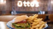   A burger and fries on a plate in front of the logo Otto's Burger © dpa Photographer: Daniel Bockwoldt 