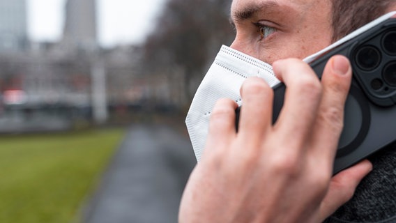Ein Mann telefoniert mit dem Smartphone und trägt eine FFP2-Maske zum Schutz vor dem Coronavirus. © picture alliance Foto: Michael Bihlmayer