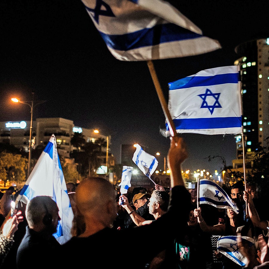Mehrere Menschen schwenken im Dunkeln israelische Fahnen. © dpa-Bildfunk Foto: Ilia Yefimovich